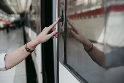 Young woman pressing button on train at railroad station - EBBF04125