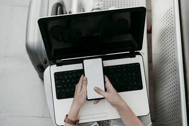 Young female passenger with laptop using mobile phone at railroad station - EBBF04153