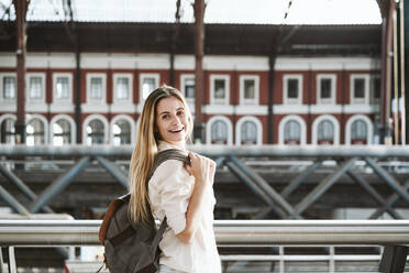 Happy blond woman wearing backpack st railroad station - EBBF04166