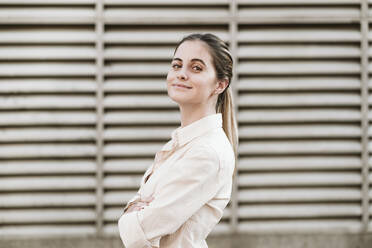 Smiling young beautiful woman standing with arms crossed - EBBF04175