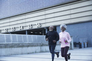 Lächelnde Frau joggt mit Mann vor einem Gebäude - PMF01938