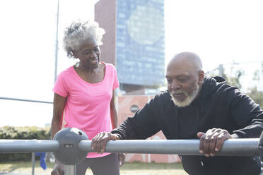 Woman looking at man exercising in park on sunny day - PMF01946