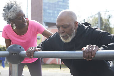 Senior woman motivating bald man exercising on railing at park - PMF01947