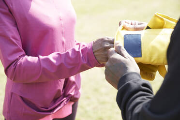 Man putting boxing glove in woman's hand on sunny day - PMF01984