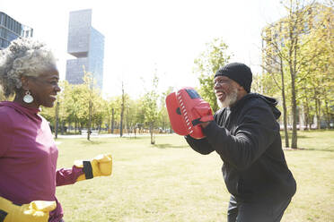 Smiling woman practicing boxing with man at park - PMF01985