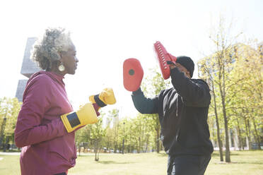 Couple with boxing gloves practicing at park during sunny day - PMF01986