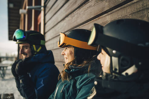 Lächelnde Freunde mit Sporthelmen im Skigebiet bei Sonnenuntergang - MASF24310