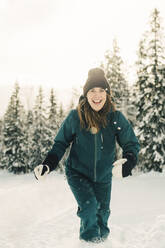 Porträt einer glücklichen Frau, die in einem Touristenort im Schnee spazieren geht - MASF24317