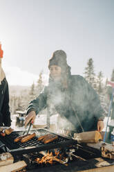 Female friends preparing sausages on barbecue grill during winter - MASF24324