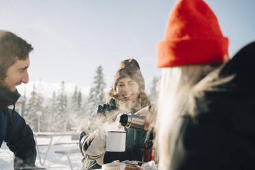 Young woman pouring coffee for female friend during winter - MASF24327