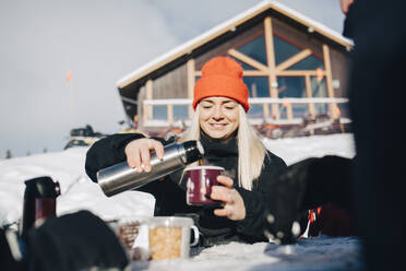 Smiling woman pouring coffee in cup during winter - MASF24329