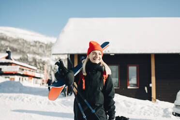 Lächelnde blonde Frau mit Ski in einem Touristenort stehend - MASF24333