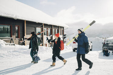 Freunde gehen in voller Länge mit Skiern in einem Touristenort an einem sonnigen Tag - MASF24340