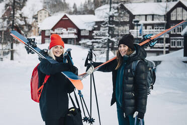 Fröhliche Freundinnen tragen Skier, während sie im Winter im Schnee stehen - MASF24352