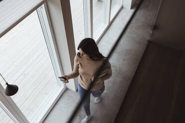 High angle view of businesswoman using smart phone while walking at home - MASF24376