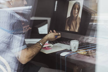 Männlicher Unternehmer in einer Videokonferenz mit einer weiblichen Kollegin am Computer durch ein Fenster gesehen - MASF24387