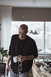 Hispanic man laughing while holding coffee mug in living room - MASF24417