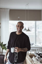 Porträt eines lächelnden Mannes mit Kaffeetasse im Wohnzimmer - MASF24421