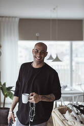 Portrait of smiling man with coffee mug in living room - MASF24421