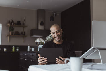 Lächelnder Geschäftsmann, der bei der Arbeit zu Hause ein digitales Tablet benutzt - MASF24433