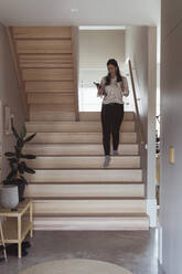 Geschäftsfrau geht die Treppe hinunter, während sie im Büro zu Hause arbeitet - MASF24456