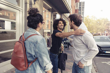 Glückliche männliche Freunde grüßen sich gegenseitig, während sie neben einer jungen Frau vor einem Café stehen - MASF24463