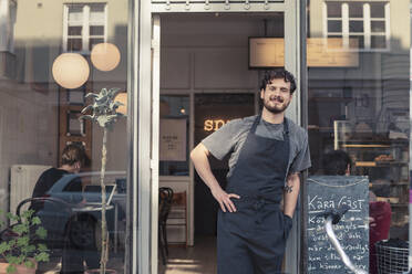 Portrait of smiling male entrepreneur leaning while standing at cafe entrance - MASF24473