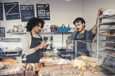 Männlicher Unternehmer diskutiert mit einem Mitinhaber, während er in einem Café in einen Notizblock schreibt - MASF24489