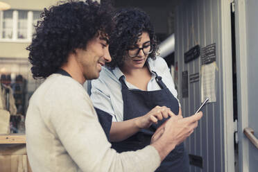 Female and male entrepreneurs using mobile phone while standing at doorway - MASF24491