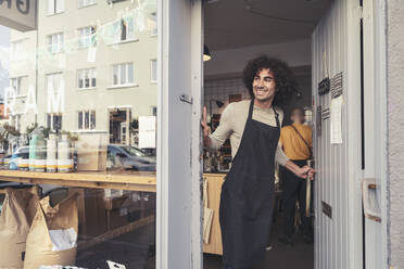 Smiling male owner opening door of organic store while looking away - MASF24496