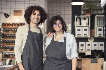 Portrait of smiling male and female entrepreneurs wearing apron standing at organic shop - MASF24499