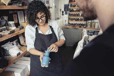 Verkäuferin zeigt einem männlichen Kunden im Bioladen eine wiederverwendbare Flasche - MASF24517