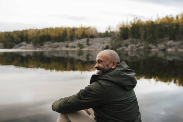 Happy male explorer looking away while spending leisure time by lake - MASF24543