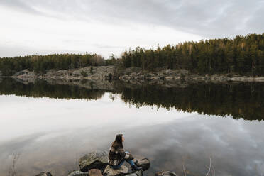 Hochformatige Ansicht einer auf einem Felsen am See sitzenden Forscherin - MASF24546