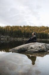 Wanderin sitzt auf einem Felsen am See gegen den Himmel - MASF24547