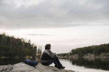Ältere Wanderin verbringt ihre Freizeit auf einem Felsen am See sitzend im Urlaub - MASF24552