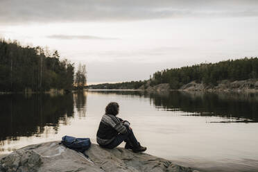 Wanderin bewundert den See, während sie auf einem Felsen gegen den Himmel sitzt - MASF24553