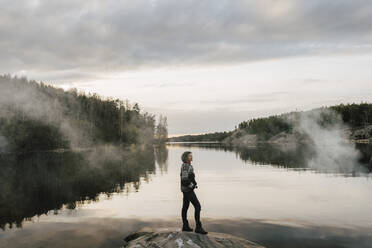 Mature female explorer standing on rock by lake - MASF24557