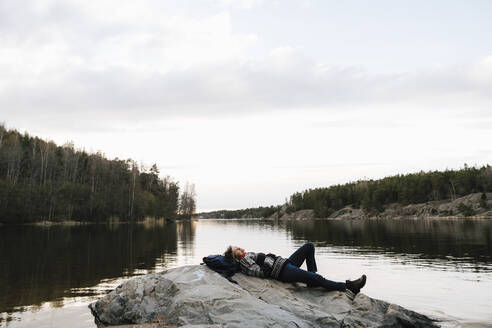 Weibliche Entdeckerin entspannt sich auf einem Felsen am See gegen den Himmel im Urlaub - MASF24560