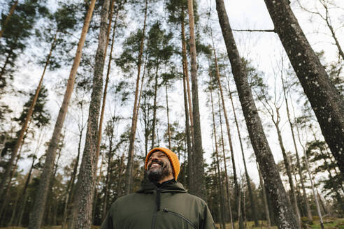 Lächelnder männlicher Wanderer im Wald vor Bäumen - MASF24562