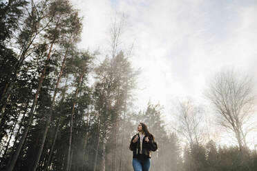 Niedriger Blickwinkel der Frau zu Fuß im Wald bei nebligem Wetter - MASF24565