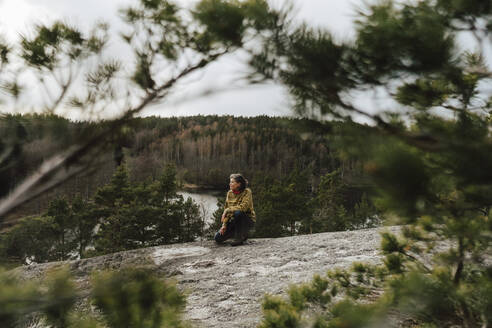 Mature female explorer kneeling on mountain against trees in forest - MASF24589