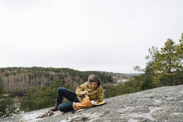 Weibliche Wanderin, die auf einem Berg liegend gegen den klaren Himmel in ihren Rucksack schaut - MASF24594
