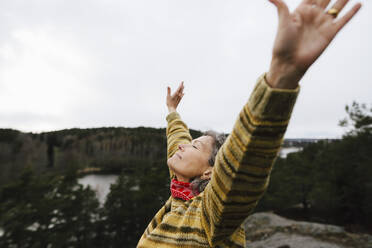 Carefree female hiker with arms raised on mountain against sky - MASF24600