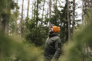 Lächelnder männlicher Wanderer, der im Wald stehend nach oben schaut - MASF24602