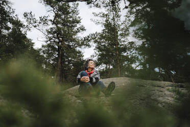 Mature woman sitting on mountain amidst tree in forest - MASF24615