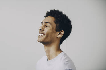Seitenansicht eines glücklichen jungen Mannes mit geschlossenen Augen vor weißem Hintergrund - MASF24626