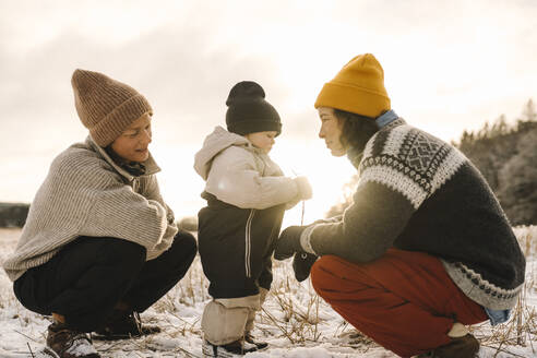 Lesbische Mütter, die bei Sonnenuntergang im Schnee bei ihrer Tochter hocken - MASF24700