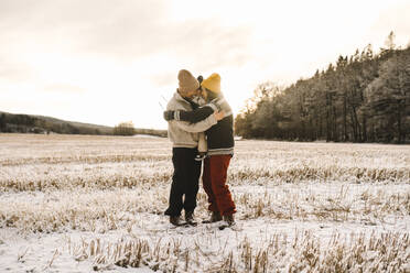 Glückliches homosexuelles Paar, das seine Tochter im Schnee stehend bei Sonnenuntergang umarmt - MASF24709