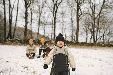 Girl wearing knit hat looking away while standing on snow - MASF24715